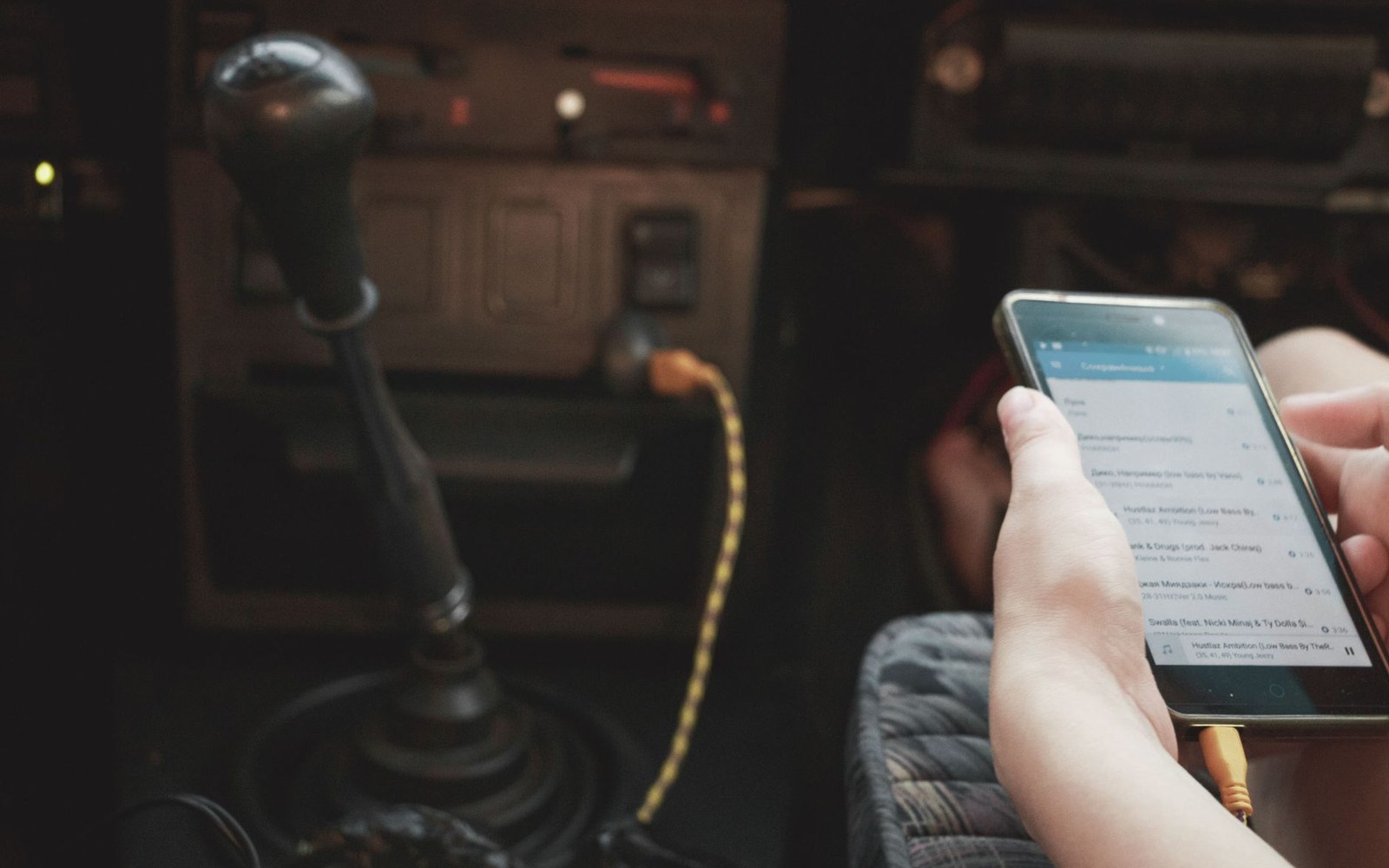 A DAB+ in-car adapter being fitted under a dashboard, adult hands at work in close frame