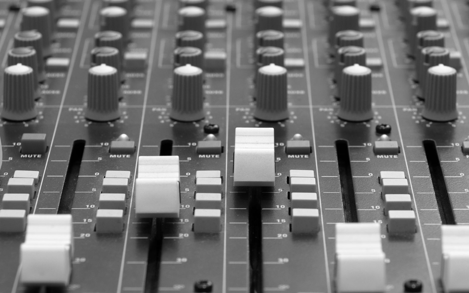 A broadcast mixing desk channel strip in close raking light, faders and meters visible