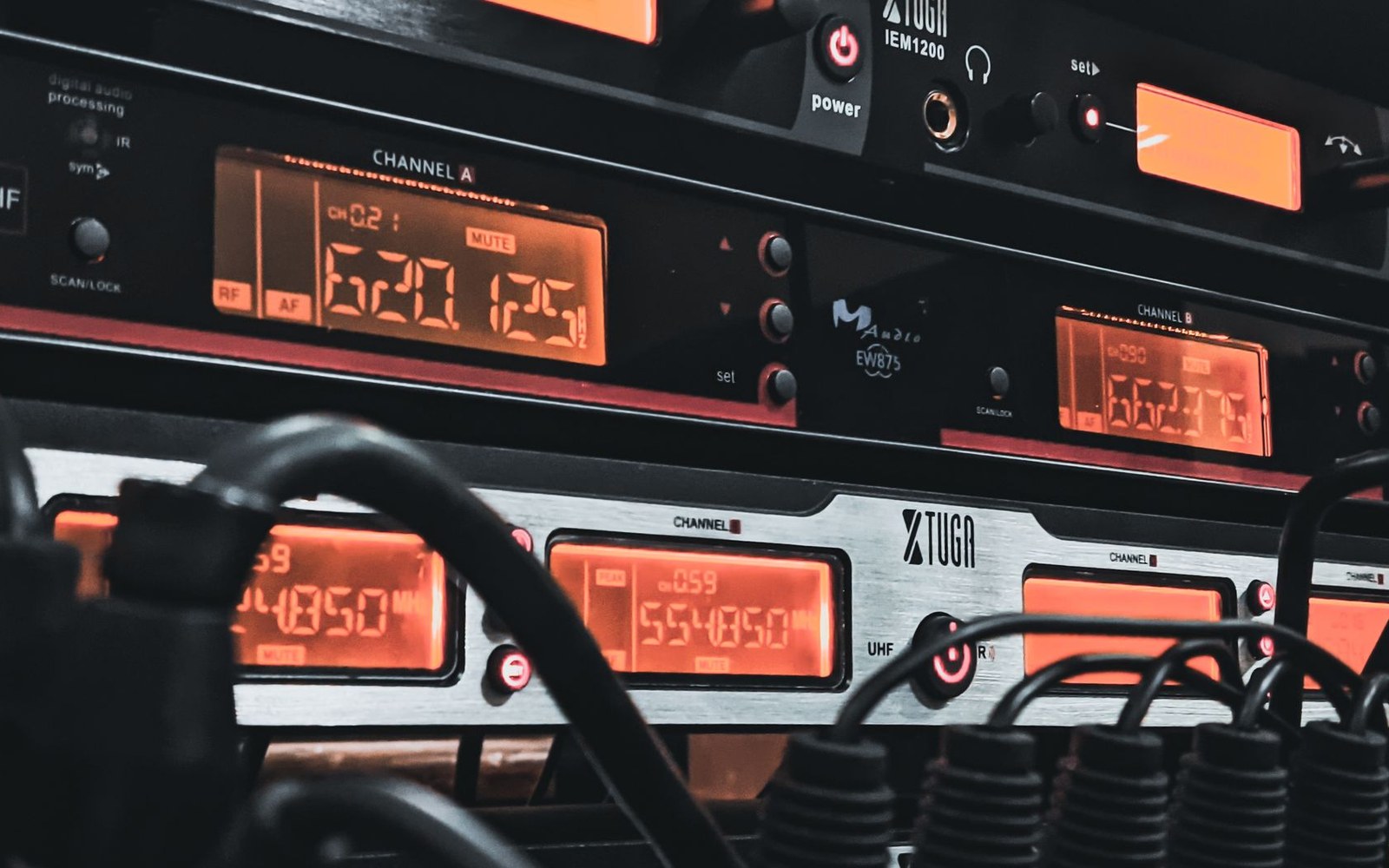 A rack of broadcast audio processing units with green and amber LEDs lit in a darkened equipment room